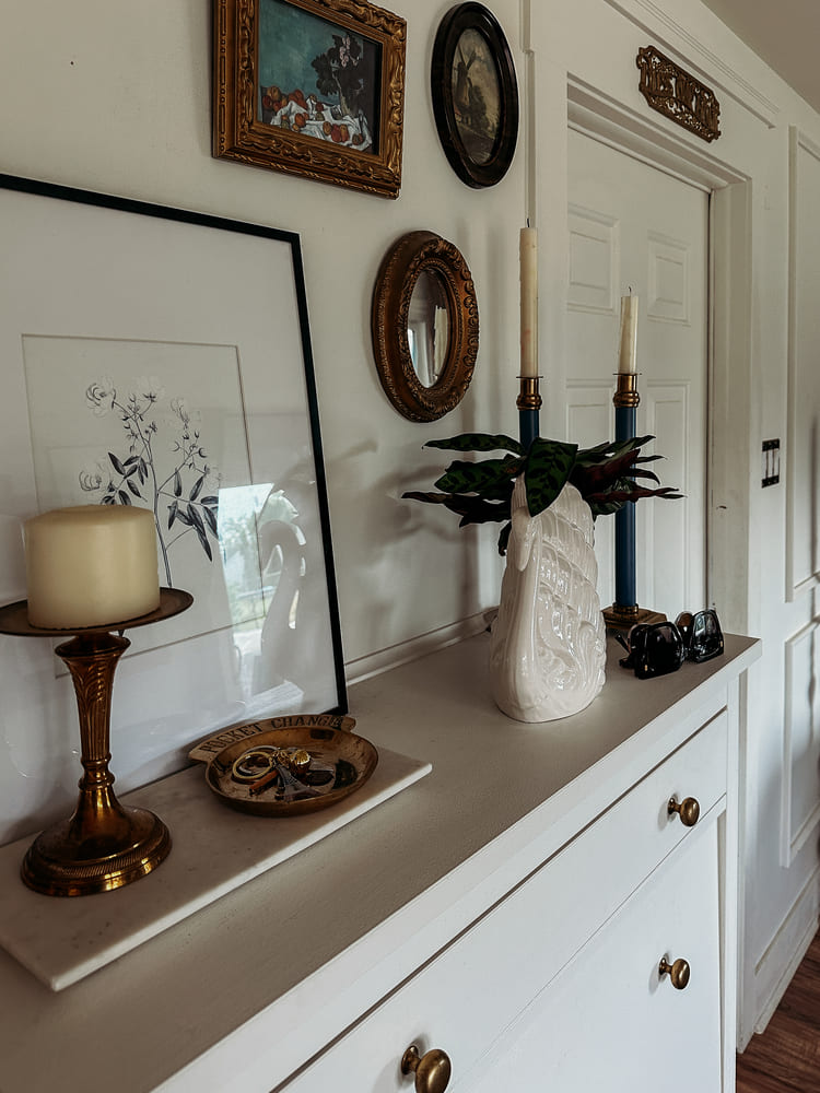 entry cabinet with thrifted vintage home decor and ornate gold frames hanging on the wall