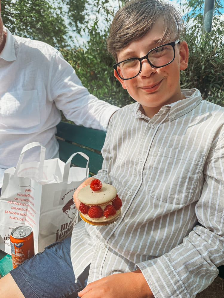 the boy holding one of the pastries in the park at the edge of Pont Neuf
