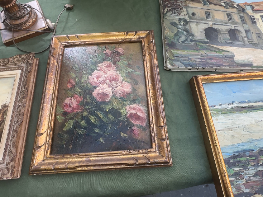 A collection of paintings and framed pictures displayed on a table, showcasing various artistic styles and subjects.