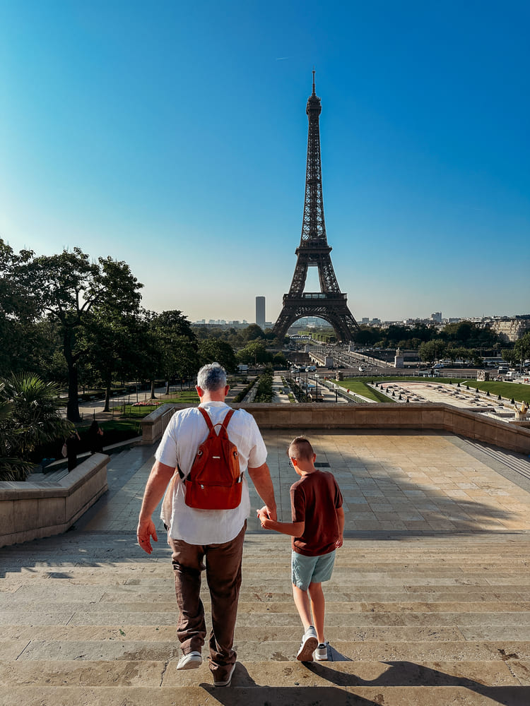 A father and son walk down the stairs with a perfect view of the Eiffel Tower.