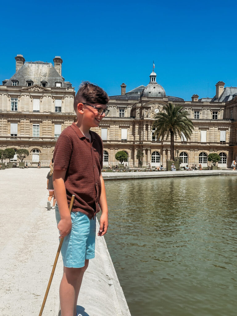 The boy is holding a stick and looking at the small boat he rented.