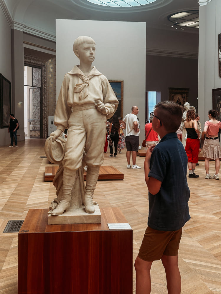 the boy is looking at the art piece in Louvre