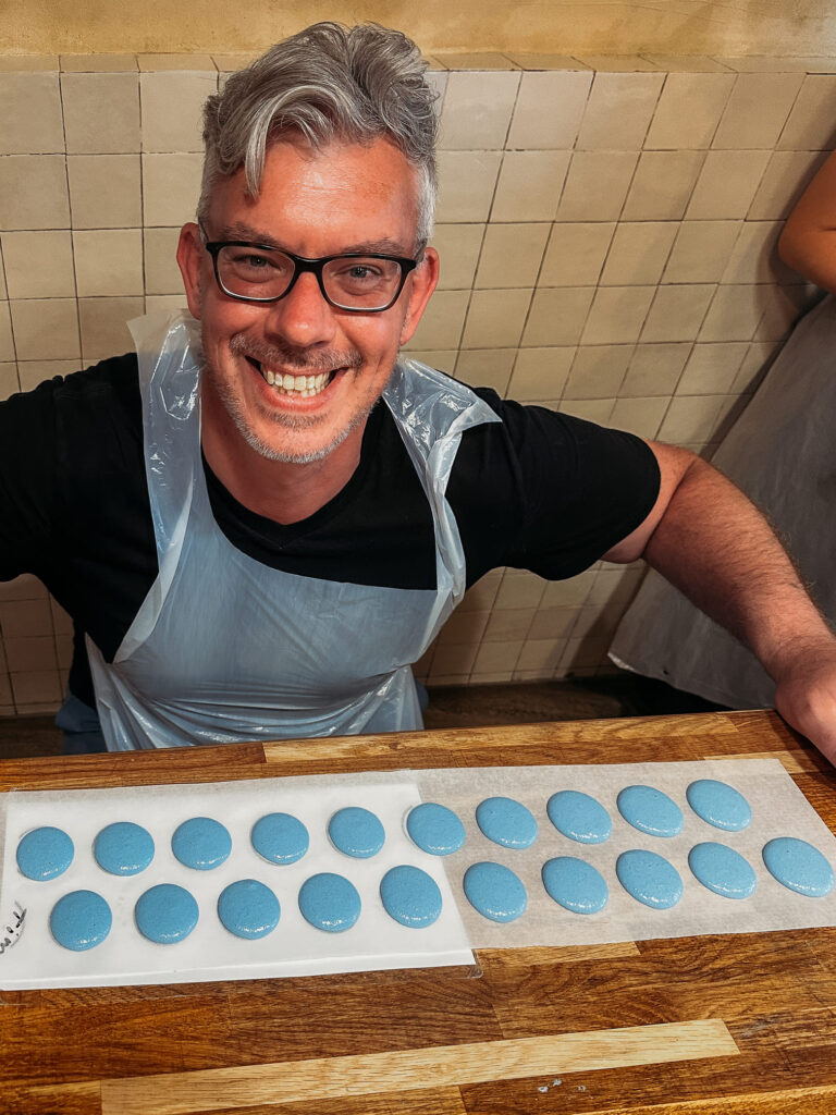 The man smiling with the macaron he made.
