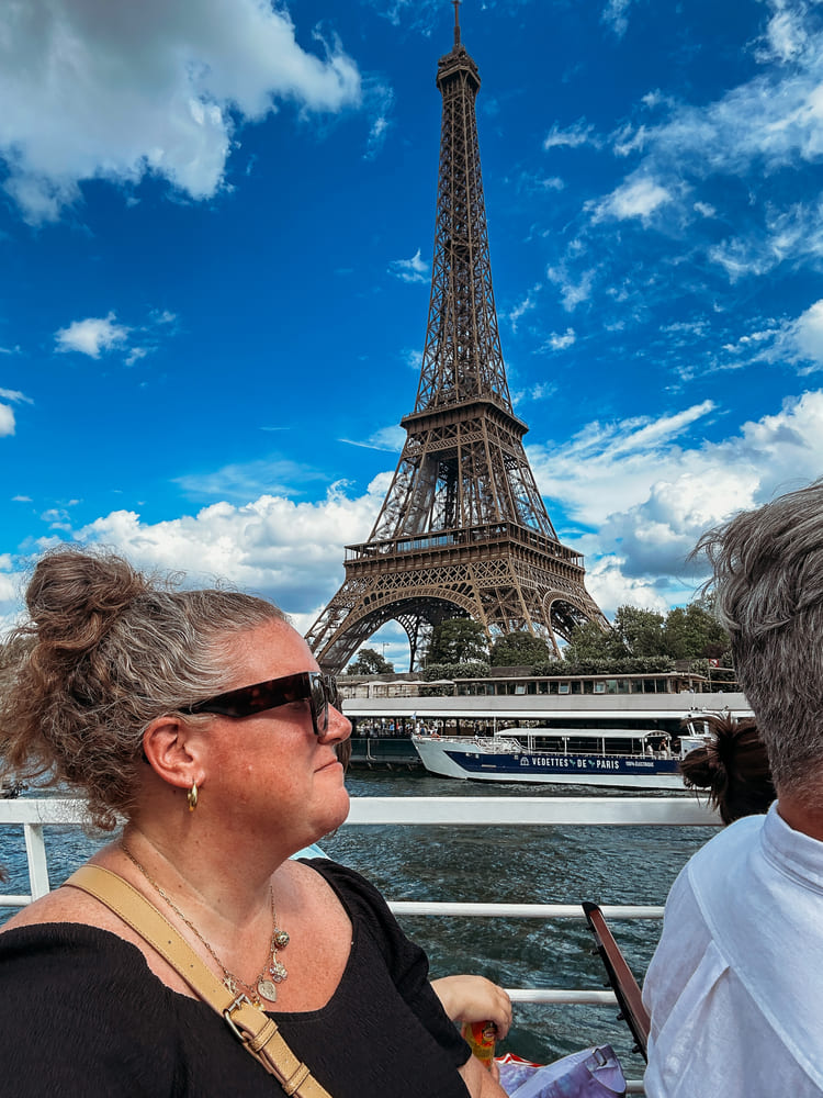 The woman is happily taking a photo beside the Eiffel Tower.