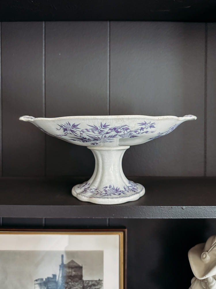 A white and blue vase compote dish on a wooden shelf, showcasing its elegant design and colors.